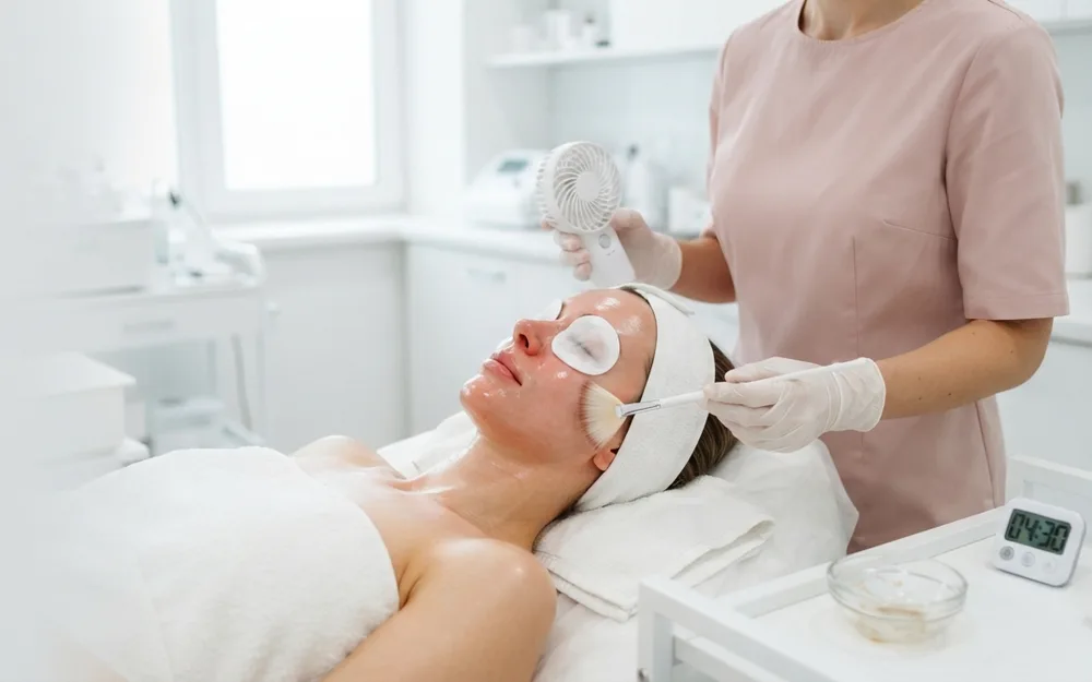 Client lying back with eye pads in place while a chemical peel is applied evenly to her forehead and cheeks